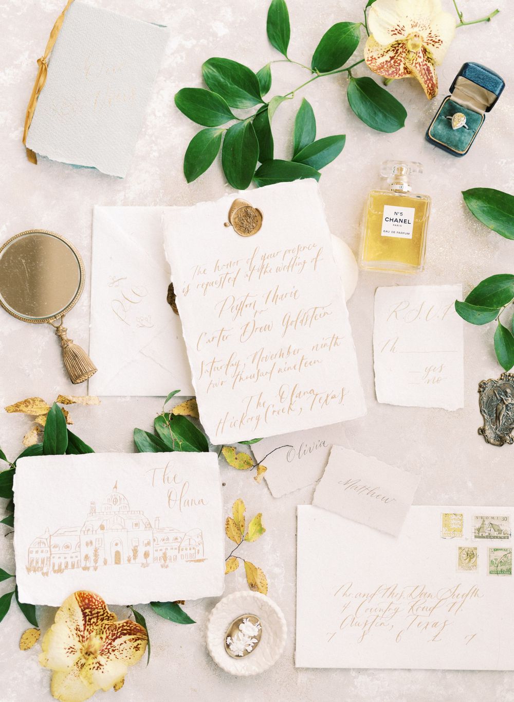 Wedding invitation suite with calligraphy, green leaves and perfume bottle on white background.