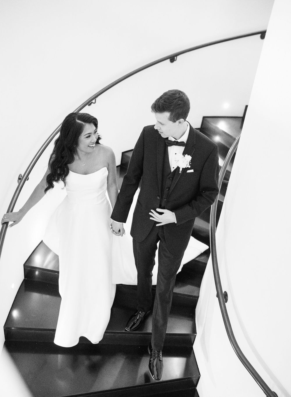 Couple descending modern curved staircase together in black and white photography.