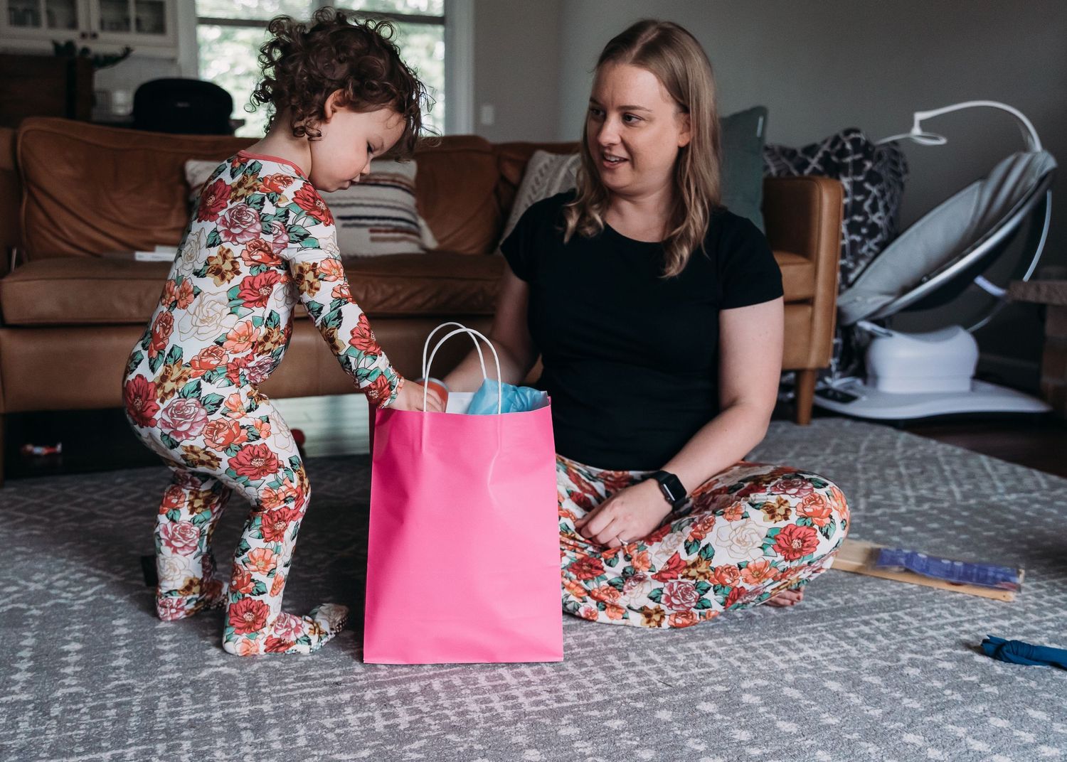 Two people in matching floral prints examine contents of a bright pink gift bag.