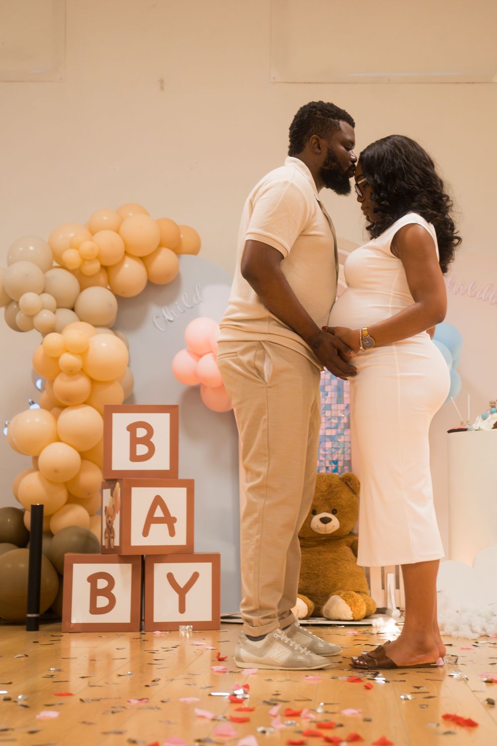 Baby announcement setup with decorative blocks spelling BABY amid balloons and rose petals.