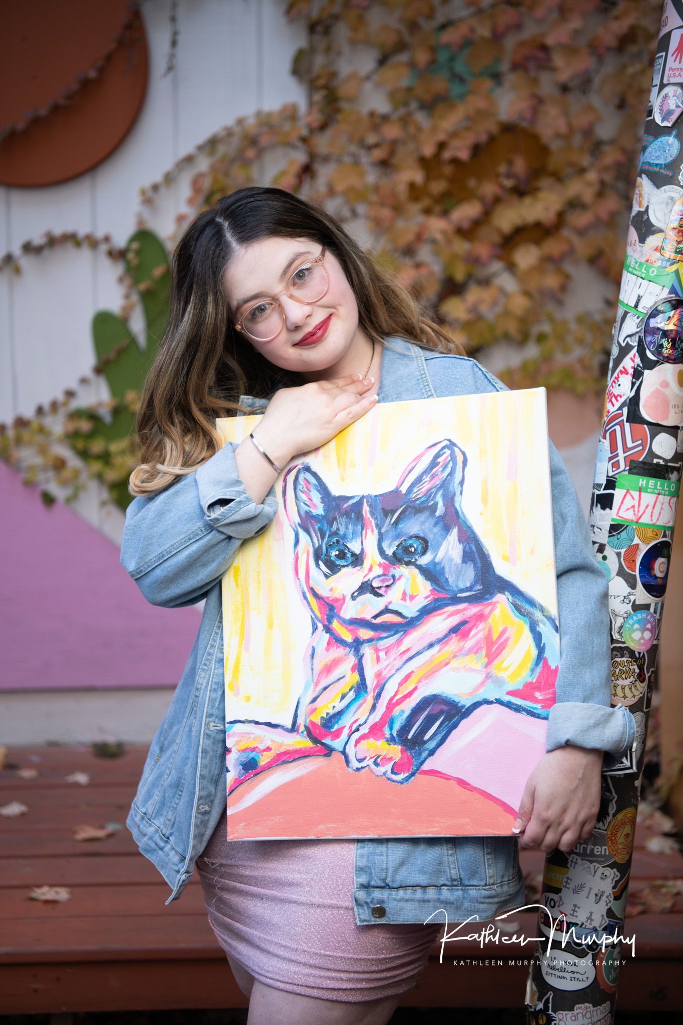 Artist showing colorful cat painting while wearing denim jacket.