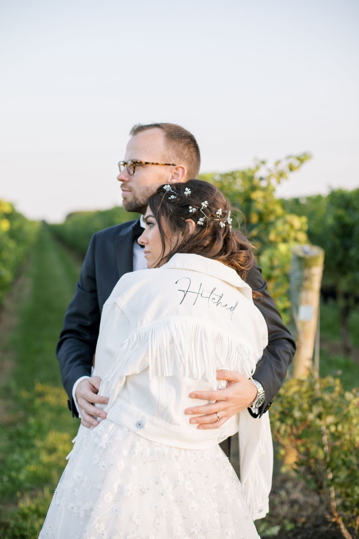 Intimate moment captured in vineyard with bride wearing white robe and floral hair accessories.