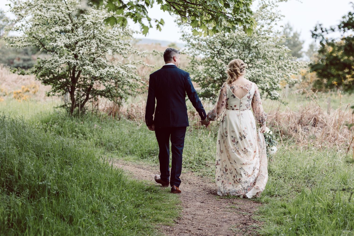 Newlyweds strolling through a blooming spring landscape with white flowering trees.
