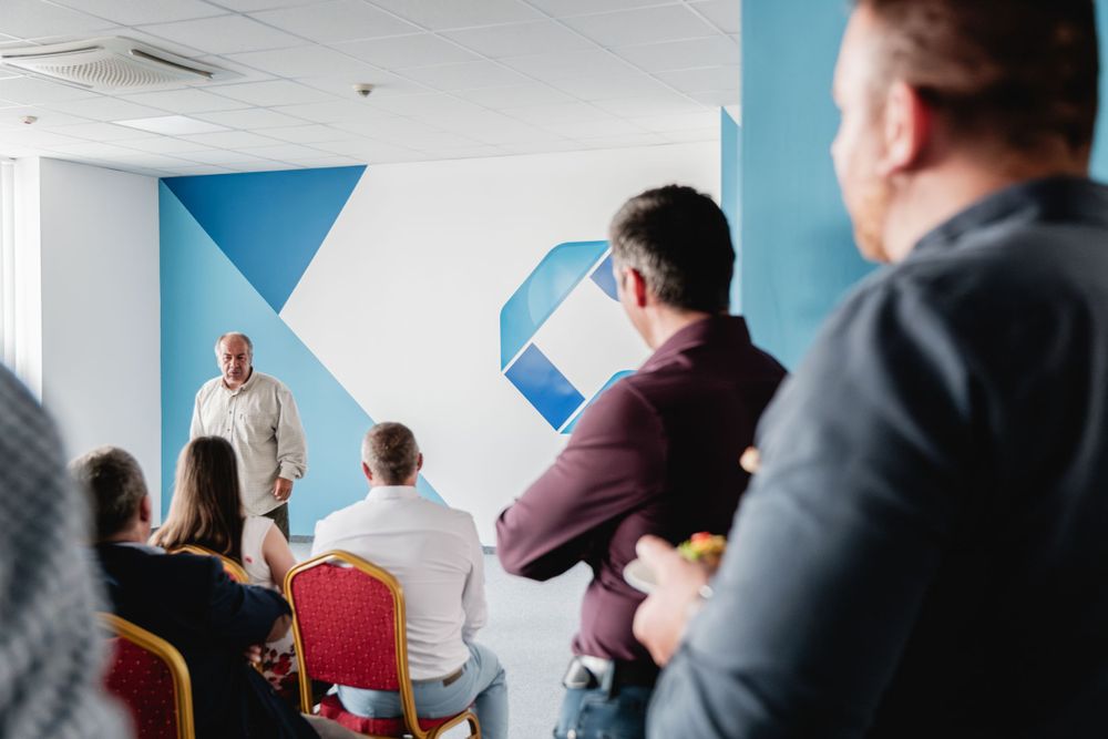 Speaker presents to attentive audience in conference room with blue geometric wall decor.