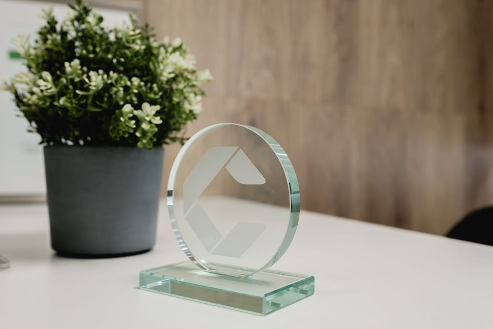 Modern glass award trophy displayed next to decorative green plant.