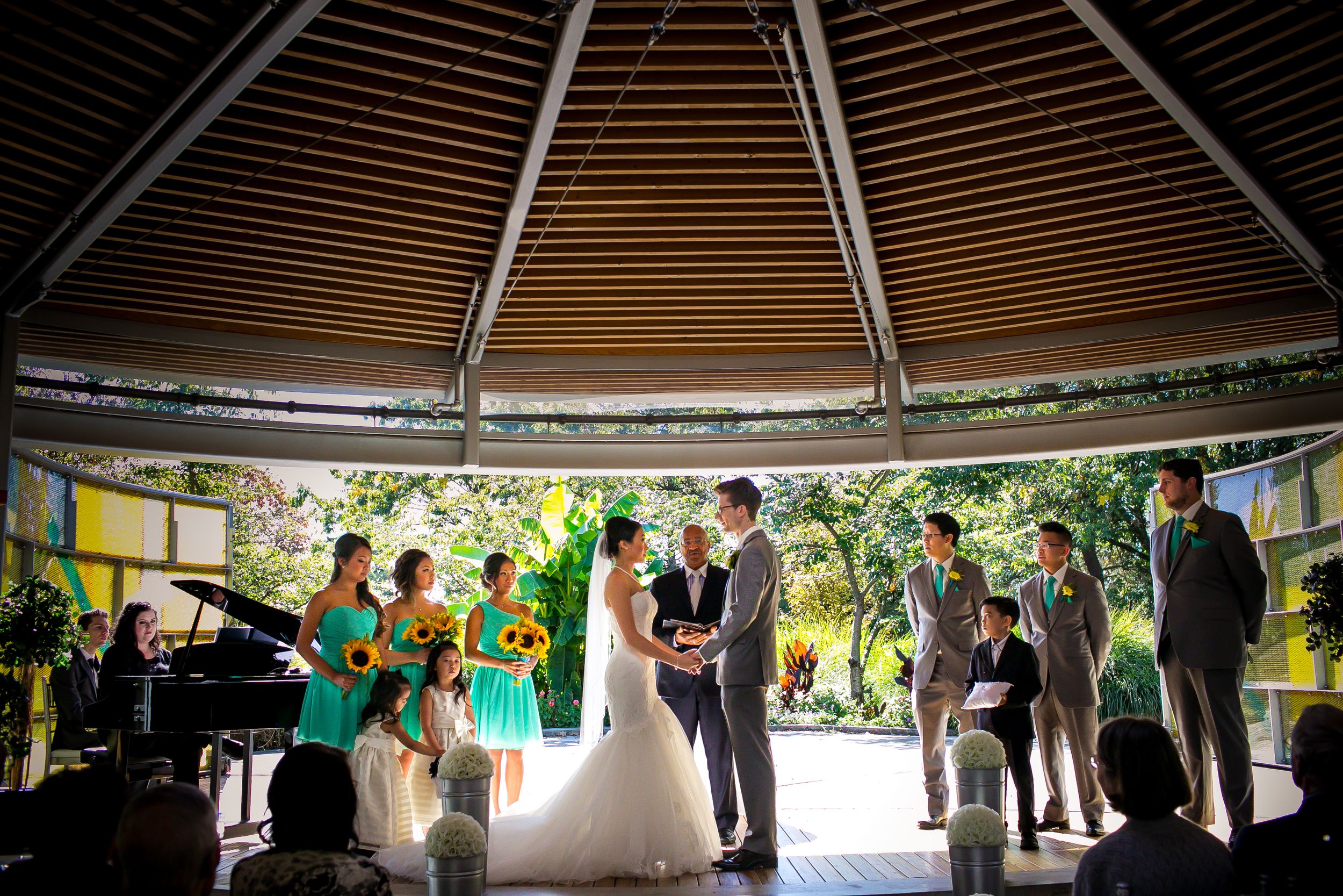 Wedding ceremony under wooden gazebo with guests gathered around couple.