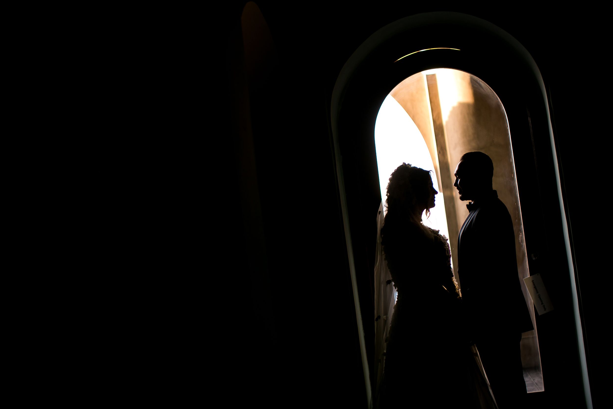 Silhouetted figures stand romantically framed within a backlit archway creating a dramatic contrast.