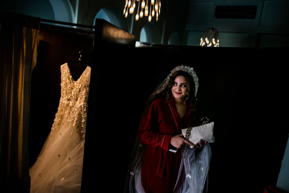Wedding dress displayed next to figure in dramatic lighting wearing red robe.