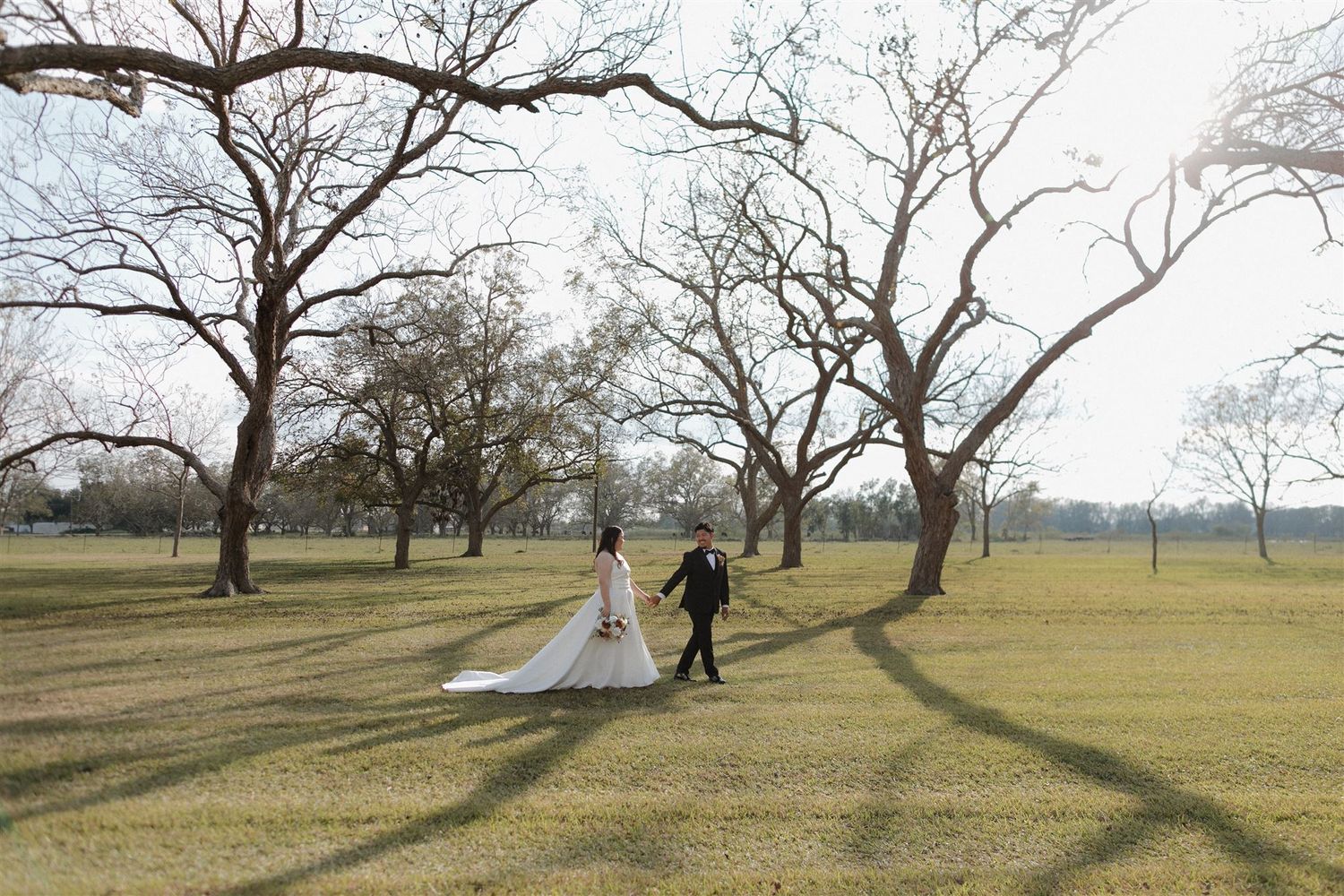 Couple strolling through a sunlit park with long shadows cast by winter trees.