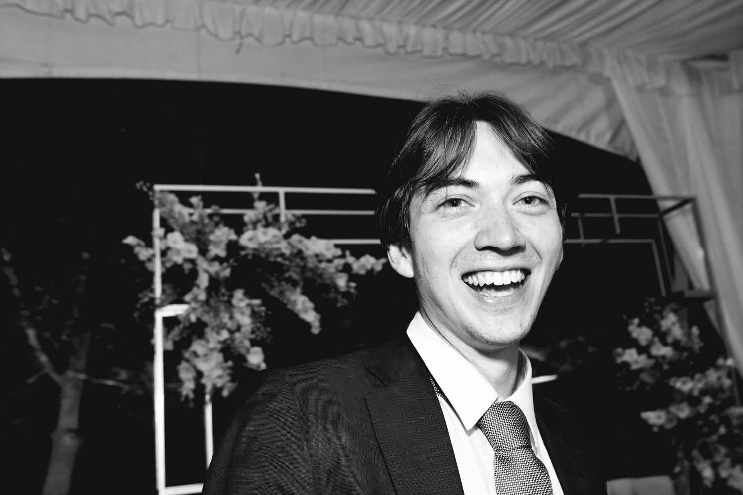 Black and white portrait showing someone in a suit laughing at a formal event.