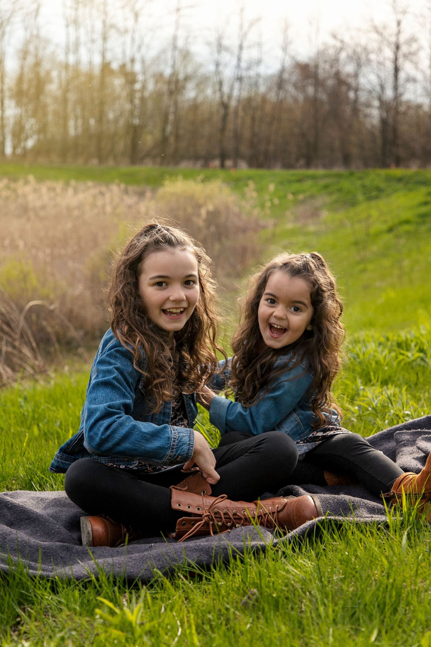2 girls in matching outfits sitting on a blanket in a grassy field