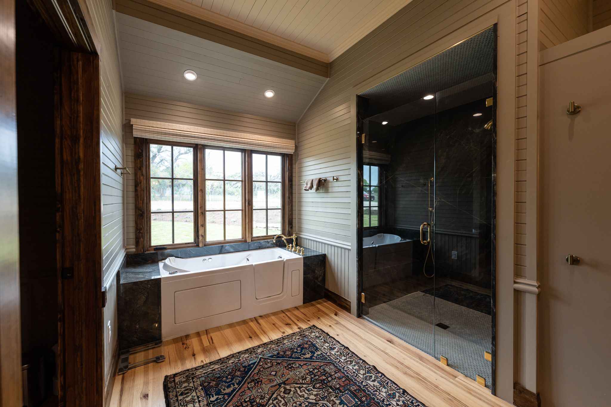 Modern bathroom interior with wood paneled walls, glass shower enclosure, and recessed lighting in luxury home design.