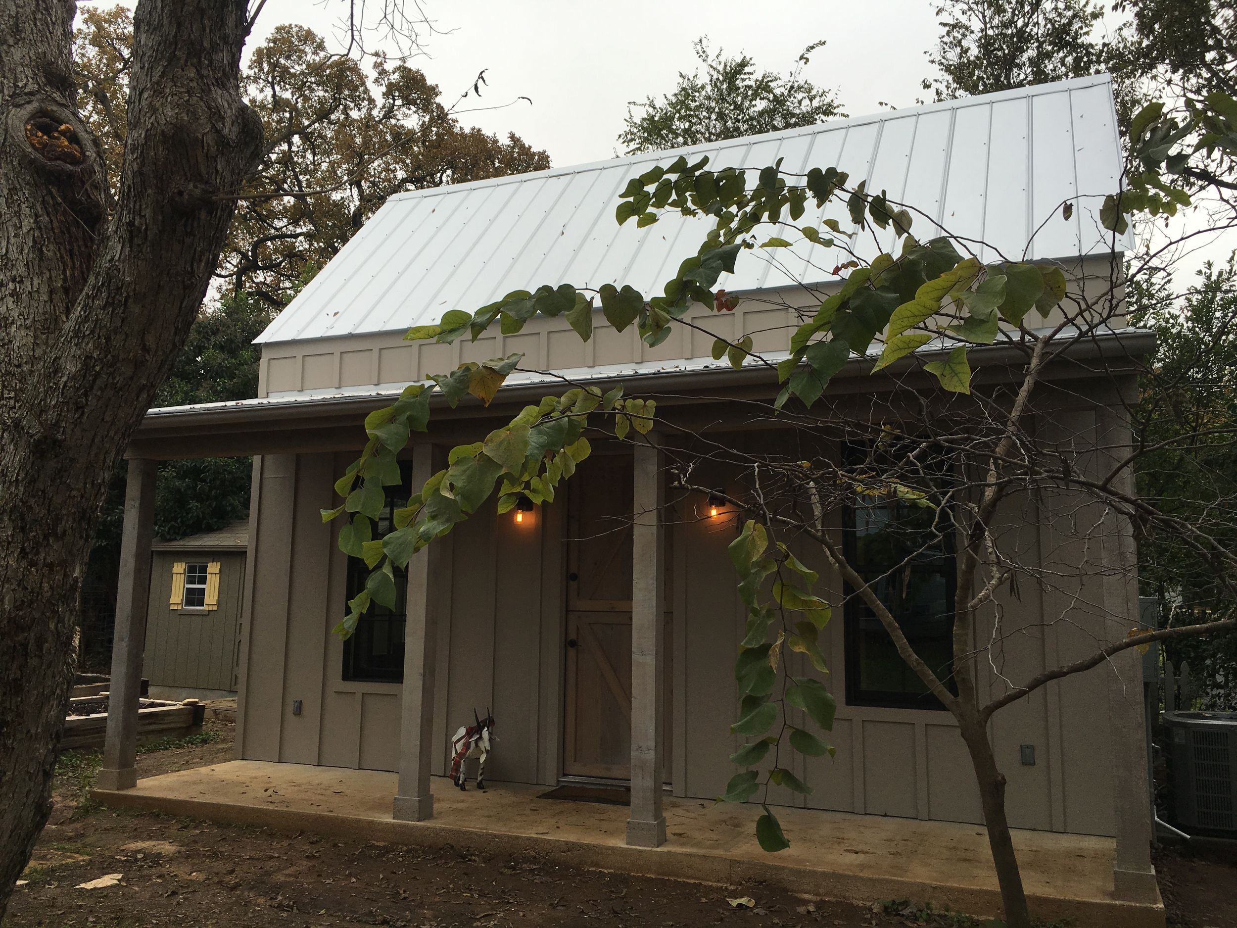 A rustic cabin with a metal roof and front porch features climbing vines and warm porch lights glowing at dusk.