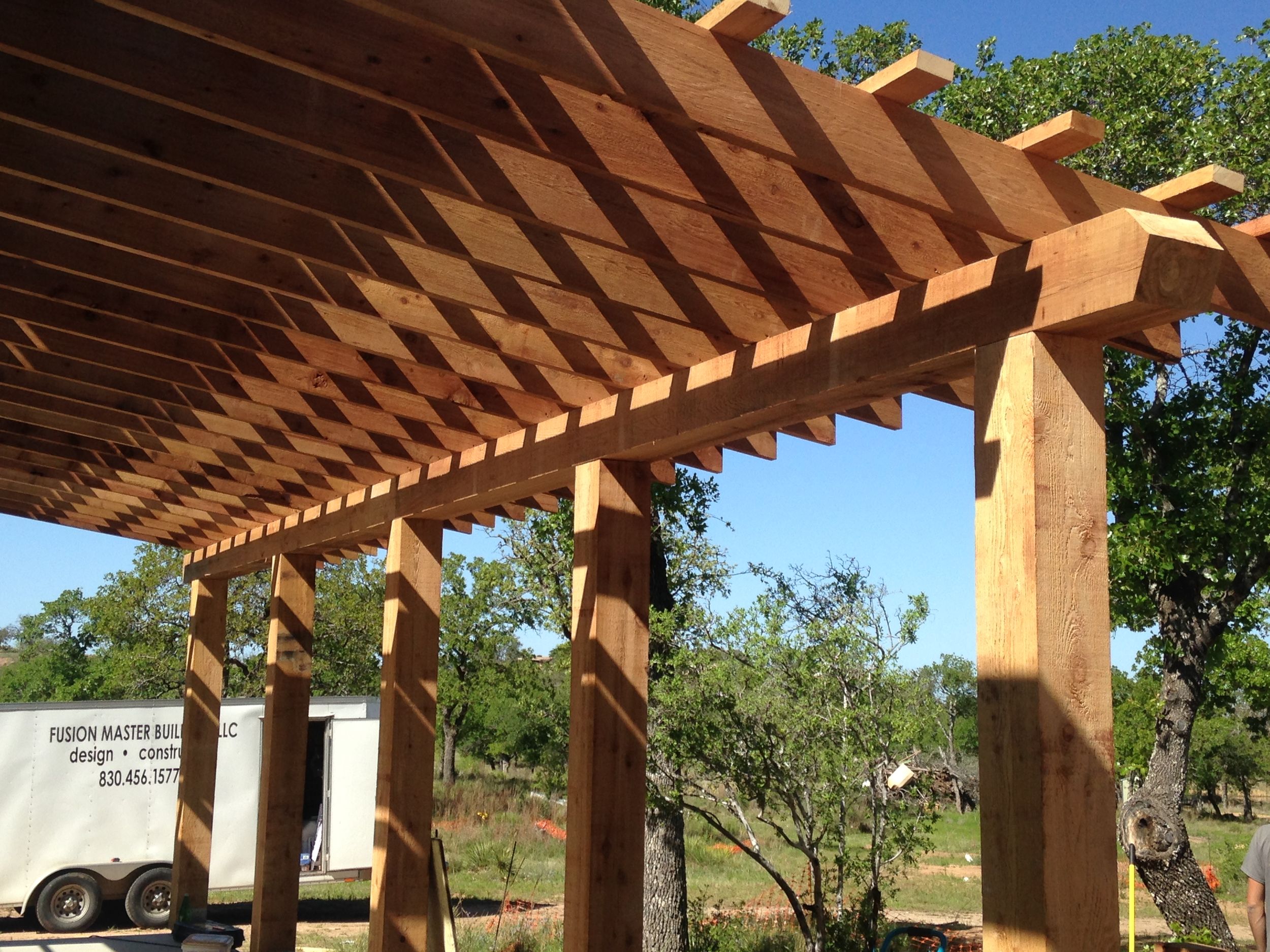 A wooden pergola structure with slatted beams creates shade and architectural interest in an outdoor garden setting.
