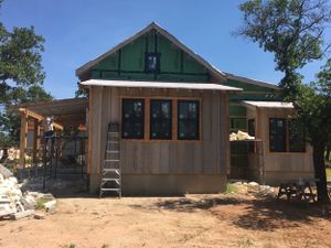 A panoramic view showing construction progress of a modern wooden cabin with green trim in a desert landscape setting.
