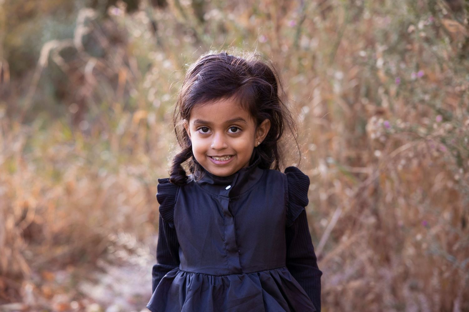Young person wearing navy blue dress with ruffles in outdoor autumn setting.
