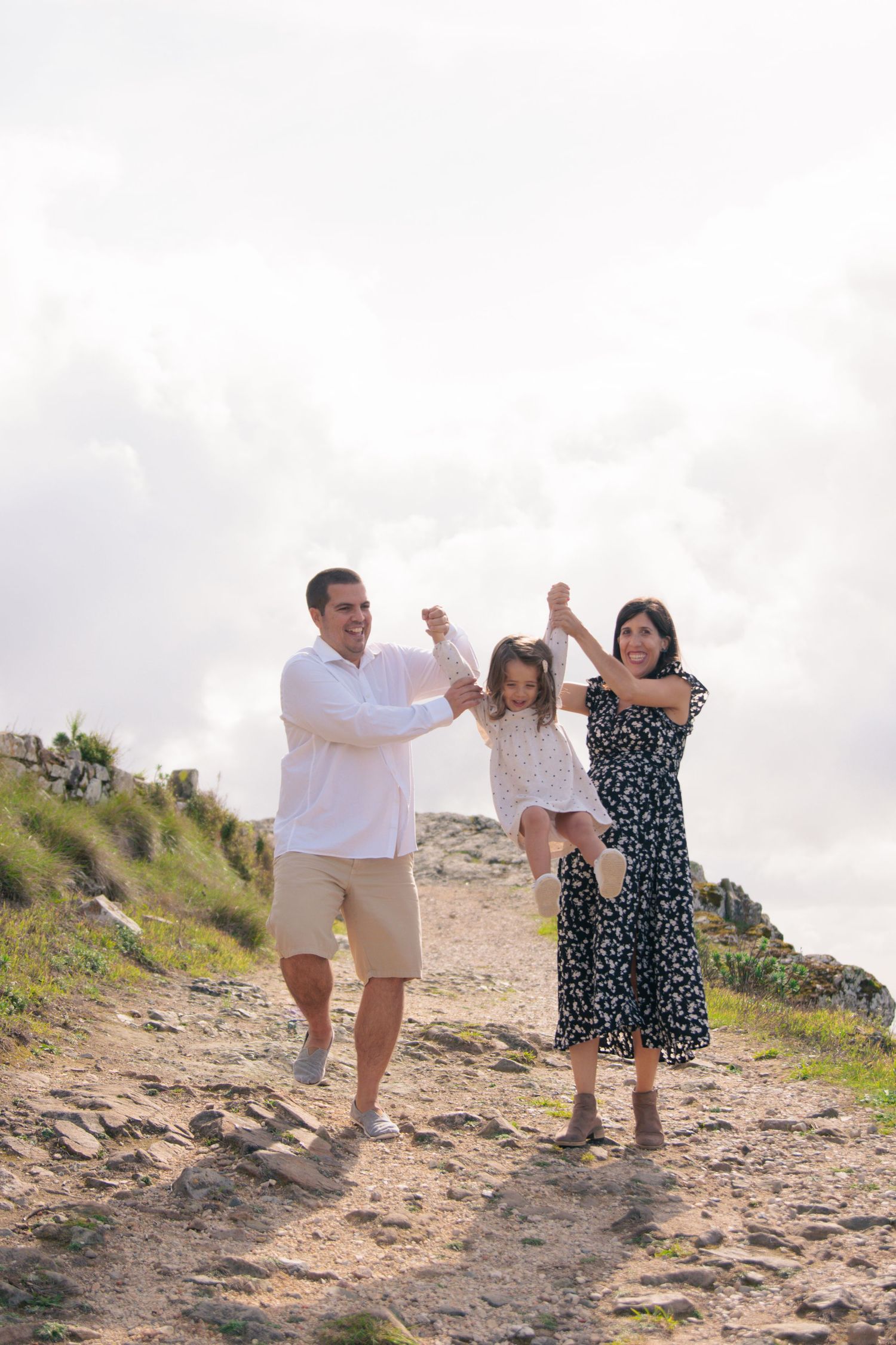 Family members hold hands while walking up a rocky hill path together.