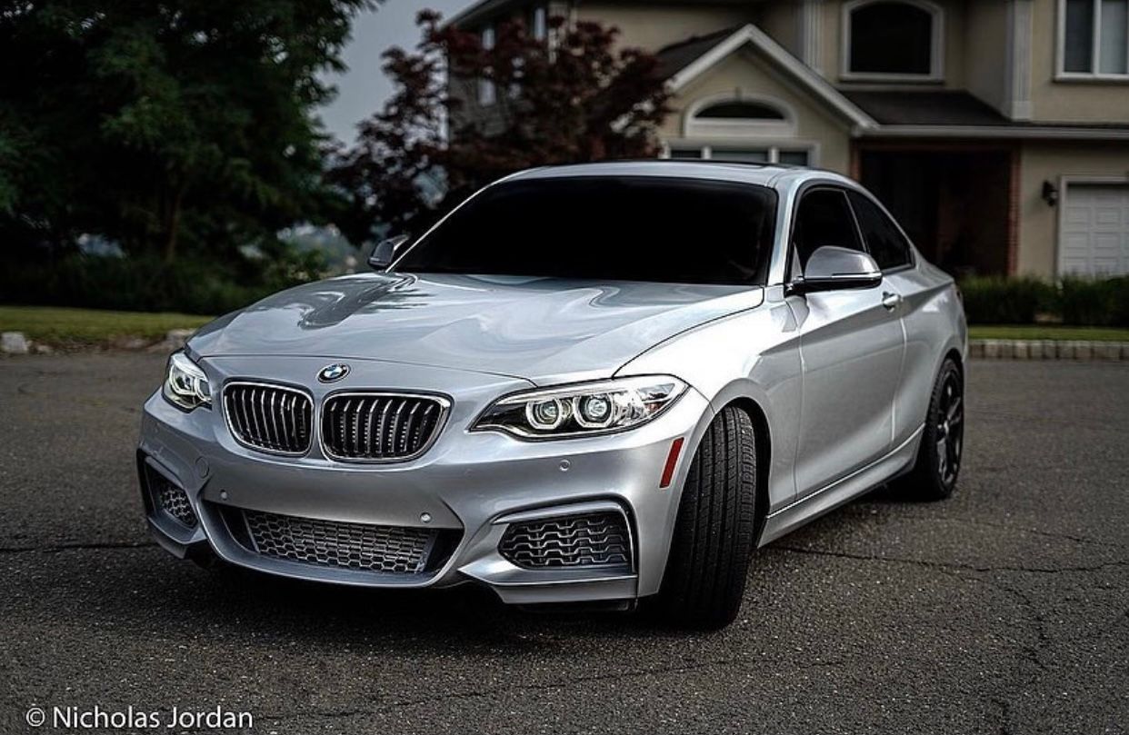 Modified silver BMW M2 with aggressive styling parked in a residential driveway.
