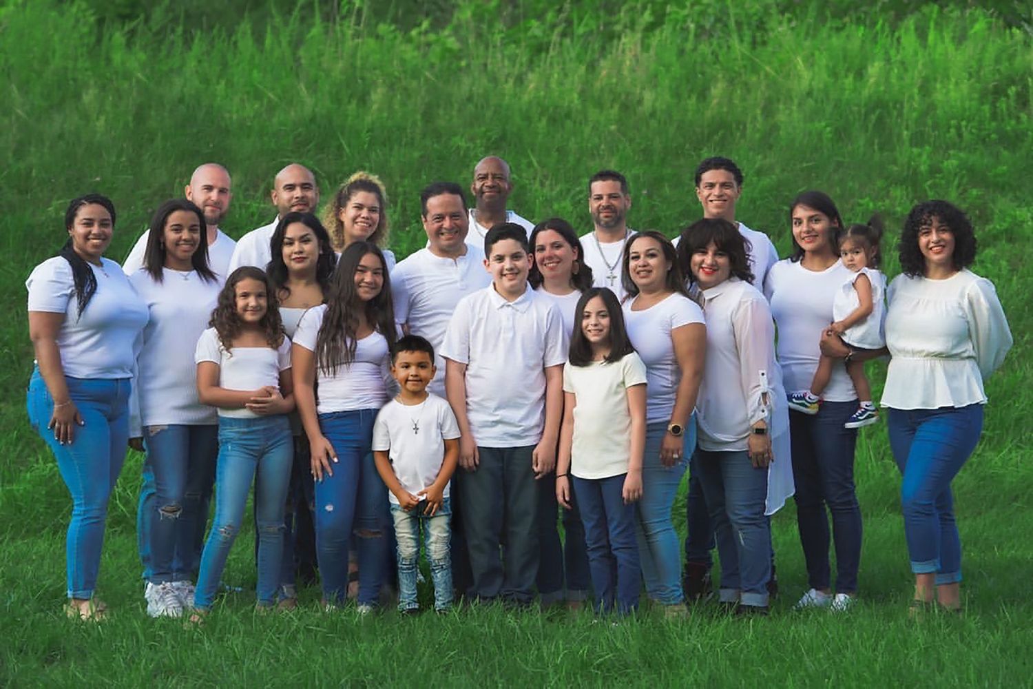 Large group gathering outdoors on grassy field wearing matching white shirts.