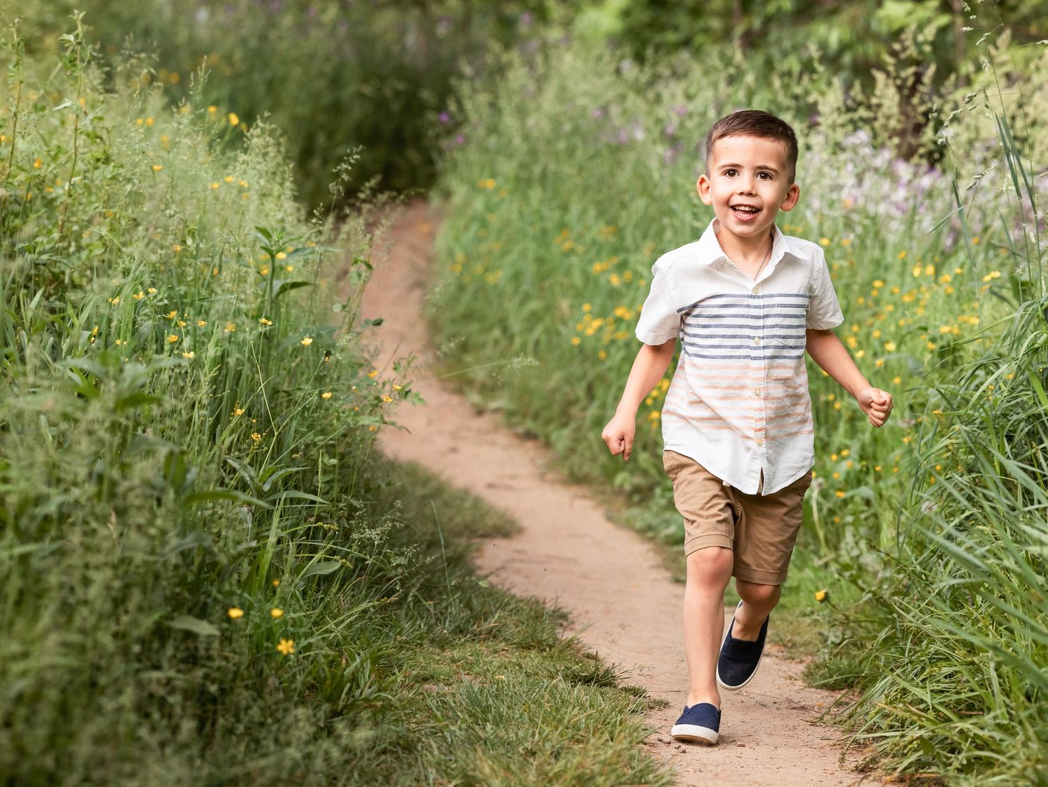 young boy running along path through tall grass and flowers during summer child photography session