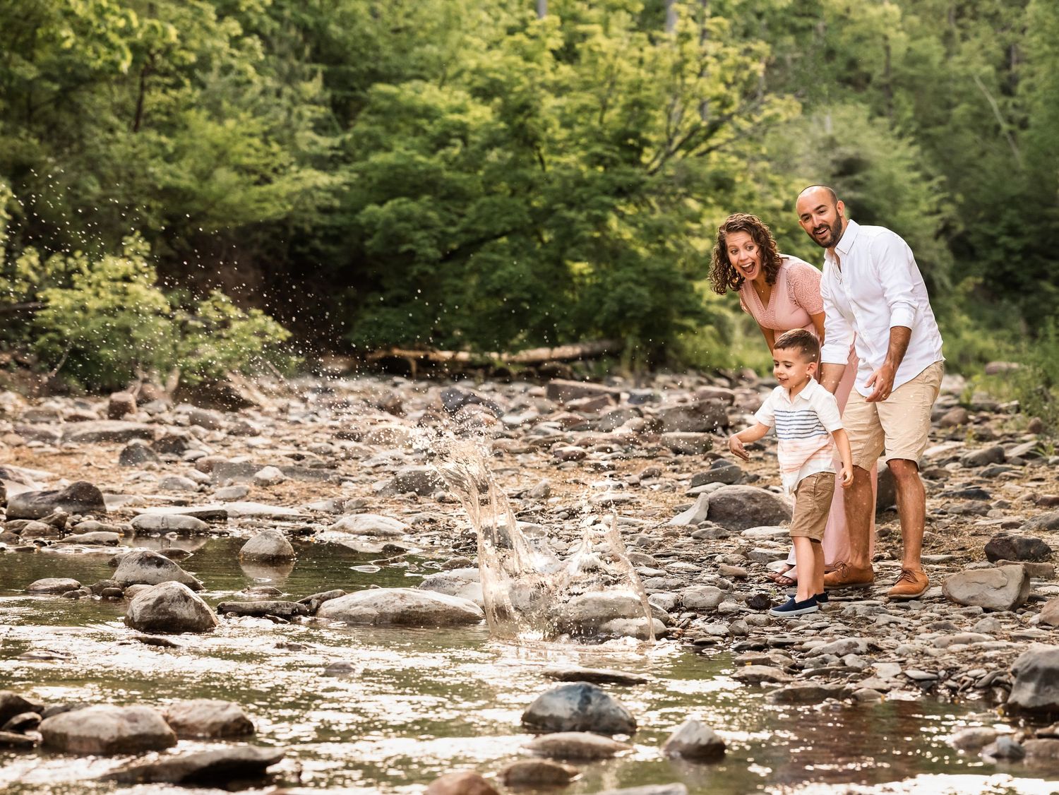 young boy skipping rocks with parents along creek during family photo session