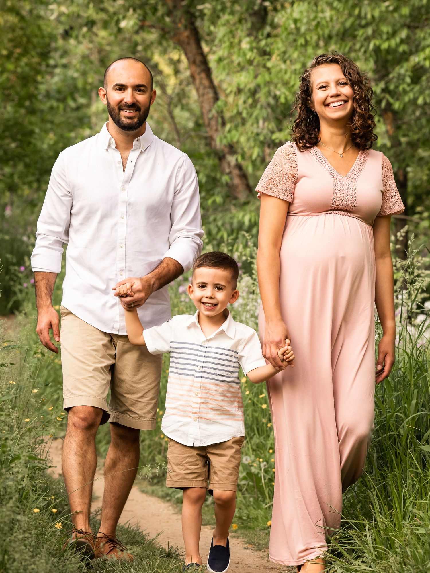 family of three walk through wildflowers at maternity photo session