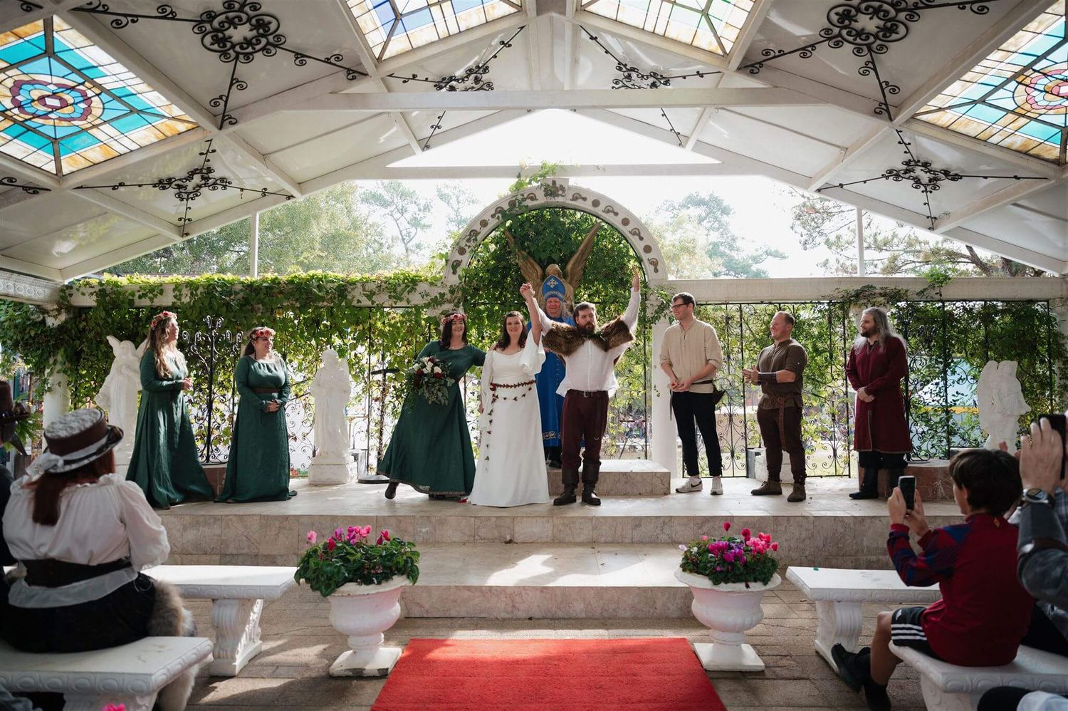 An overhead view of a medieval-themed wedding ceremony in a pavilion decorated with floral arches.
