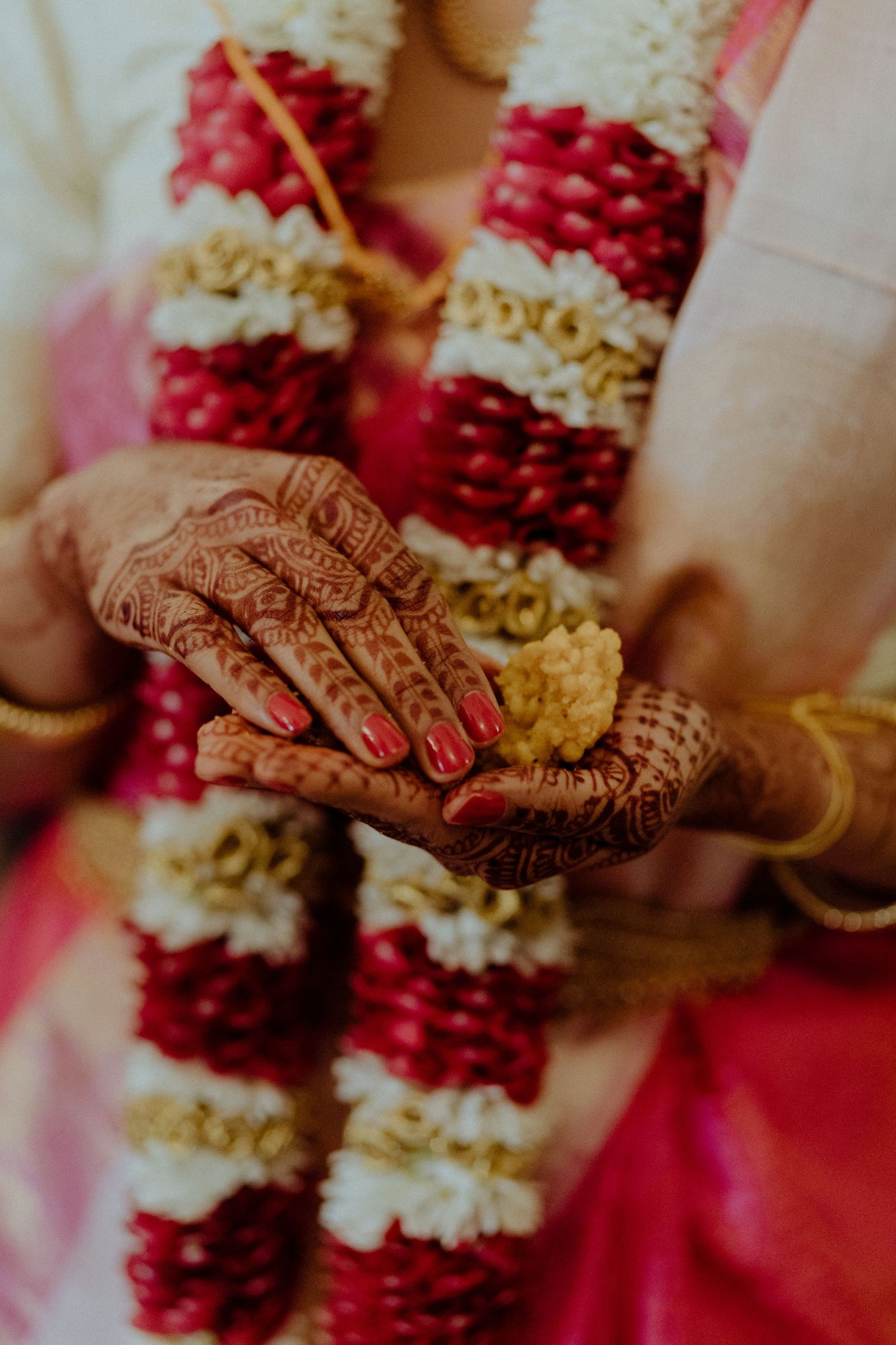 Intricate henna-adorned hands of an Indian bride holding a flower during a traditional Hindu wedding ceremony.
