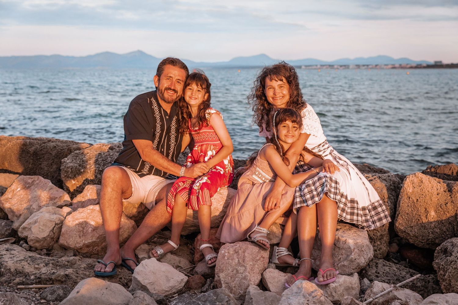 A happy family sitting on coastal rocks during a lifestyle family photo session in Mallorca.