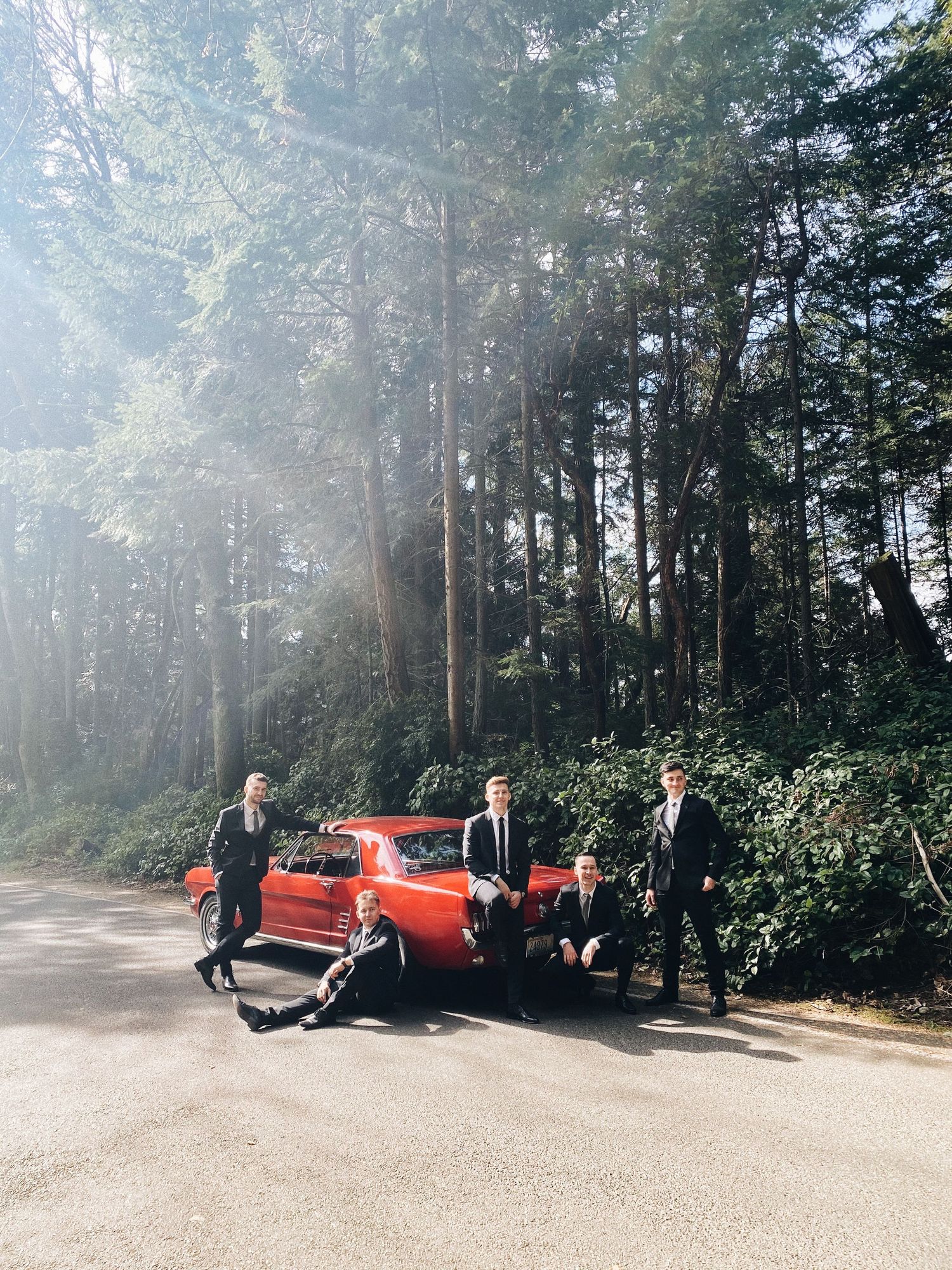 Vintage red car parked on a misty forest road with well-dressed group gathering around it.