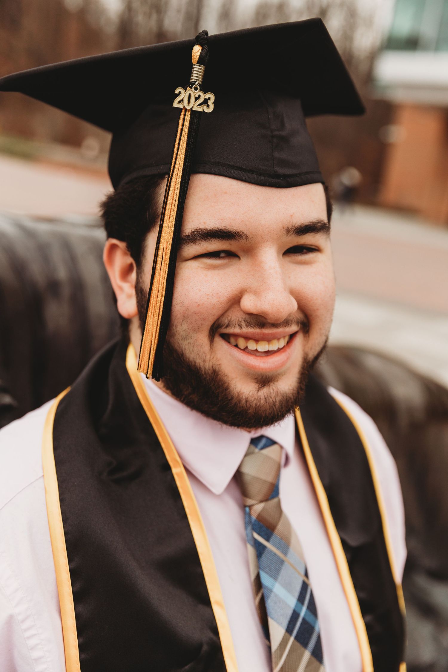 Graduate wearing black cap and gown with gold tassel and striped tie.