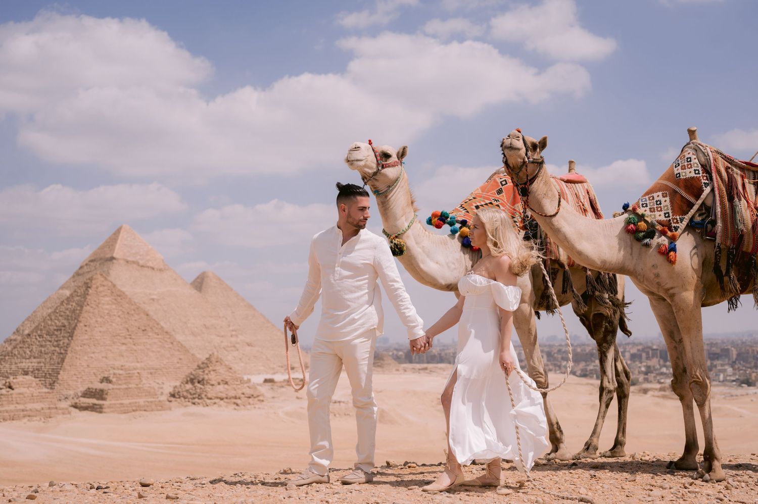 A couple poses with camels in front of the Great Pyramids of Giza in Egypt.