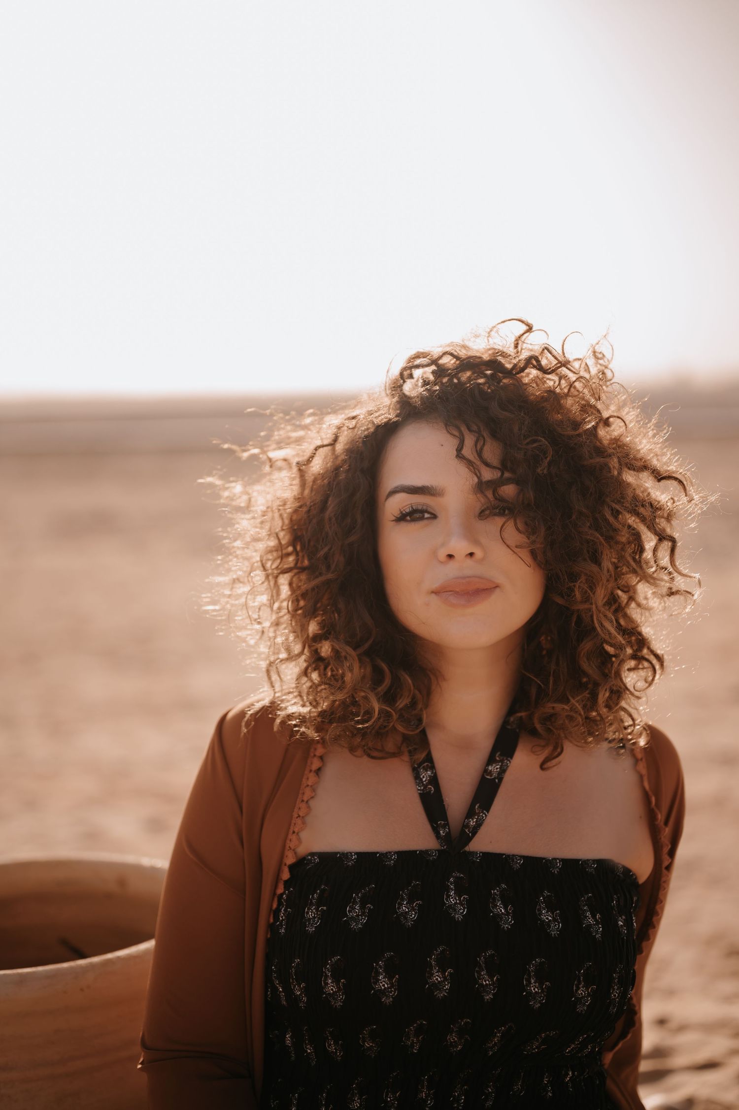 Portrait of a woman with curly hair against a desert background in warm sunlight.