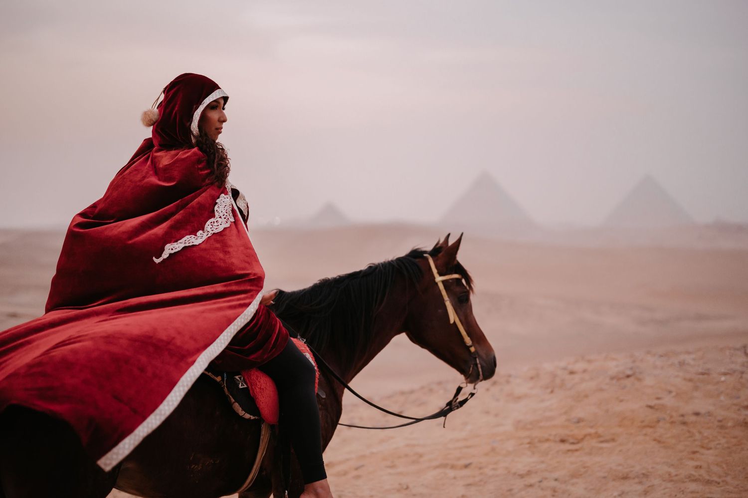 Figure in red cloak riding horseback against the backdrop of Egyptian pyramids.