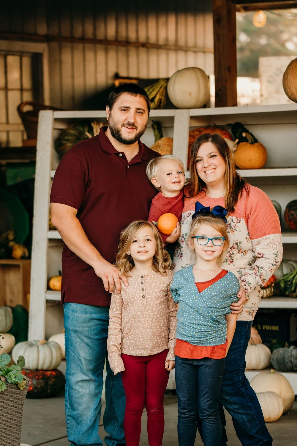 Family group portrait in front of pumpkin display wearing coordinated fall colors.