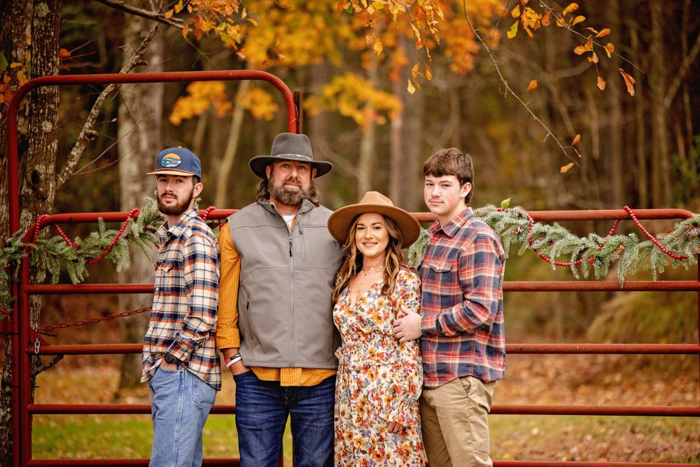 Family posing together against rustic red fence during autumn photo session.