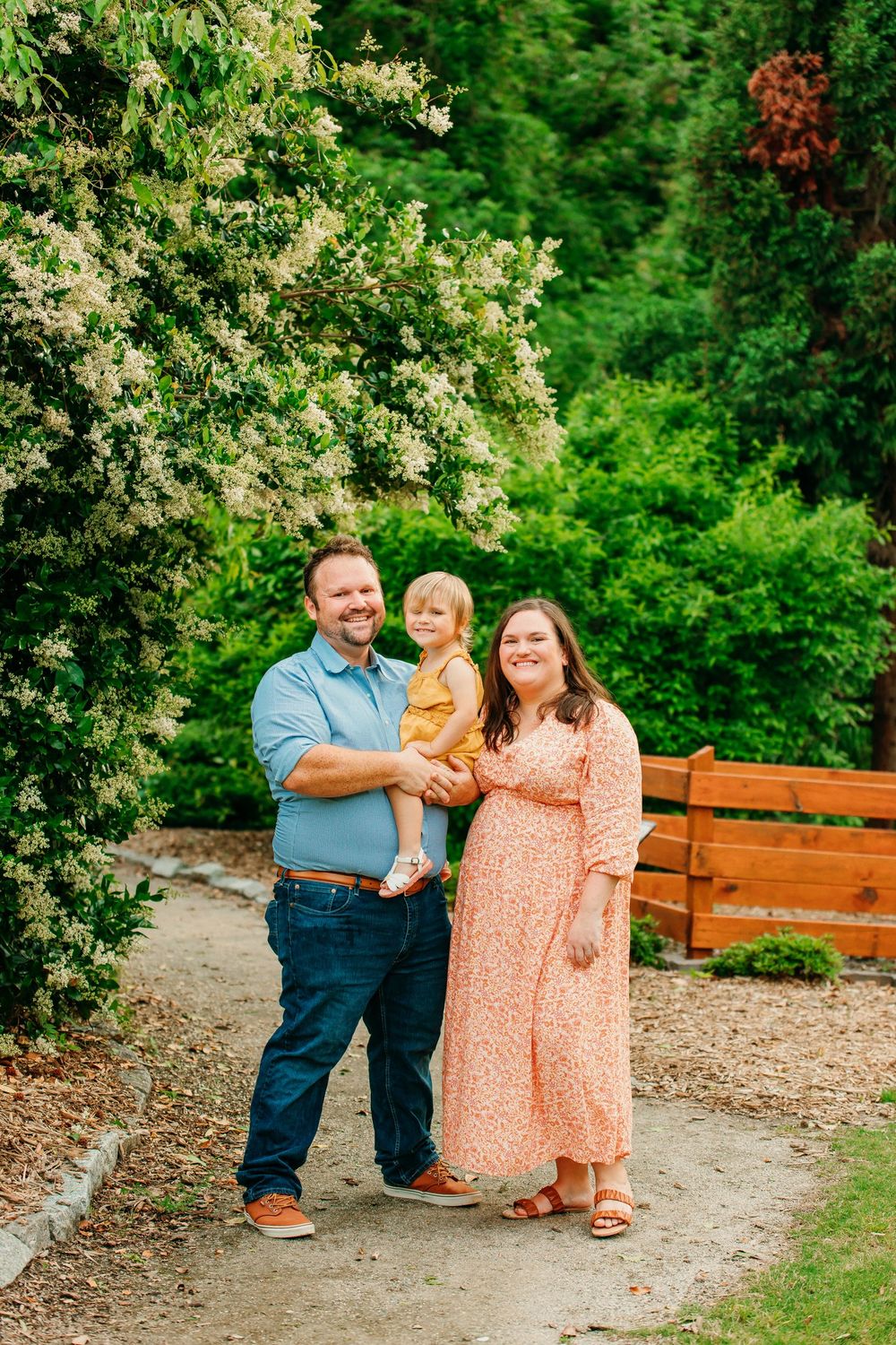 Family portrait in a lush green garden setting with wooden bench.