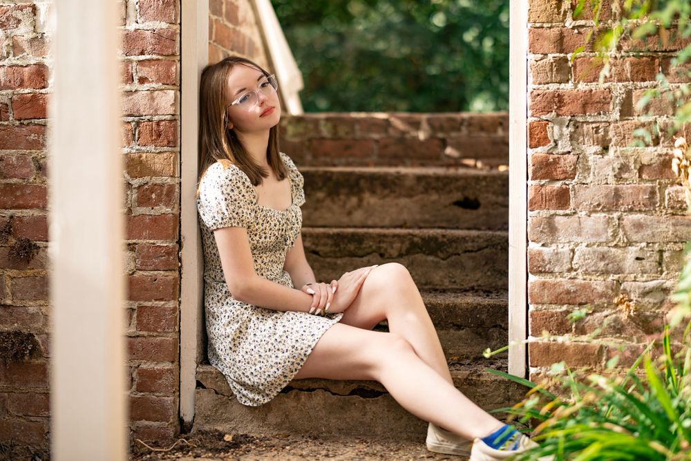 A person in a patterned dress sits on brick steps in a garden setting.