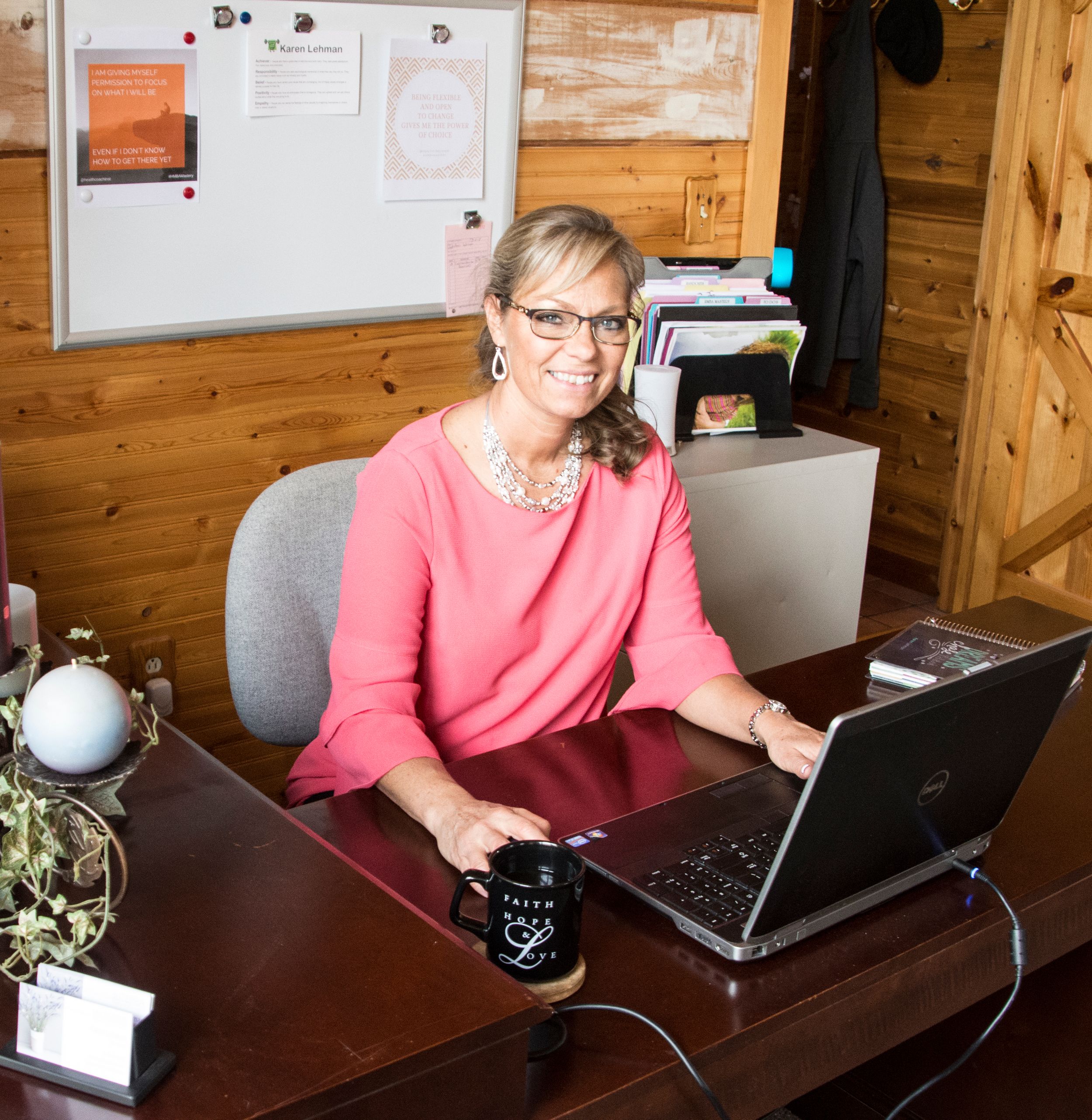 A home office setting with wooden walls showing someone at work on a laptop with office supplies nearby.