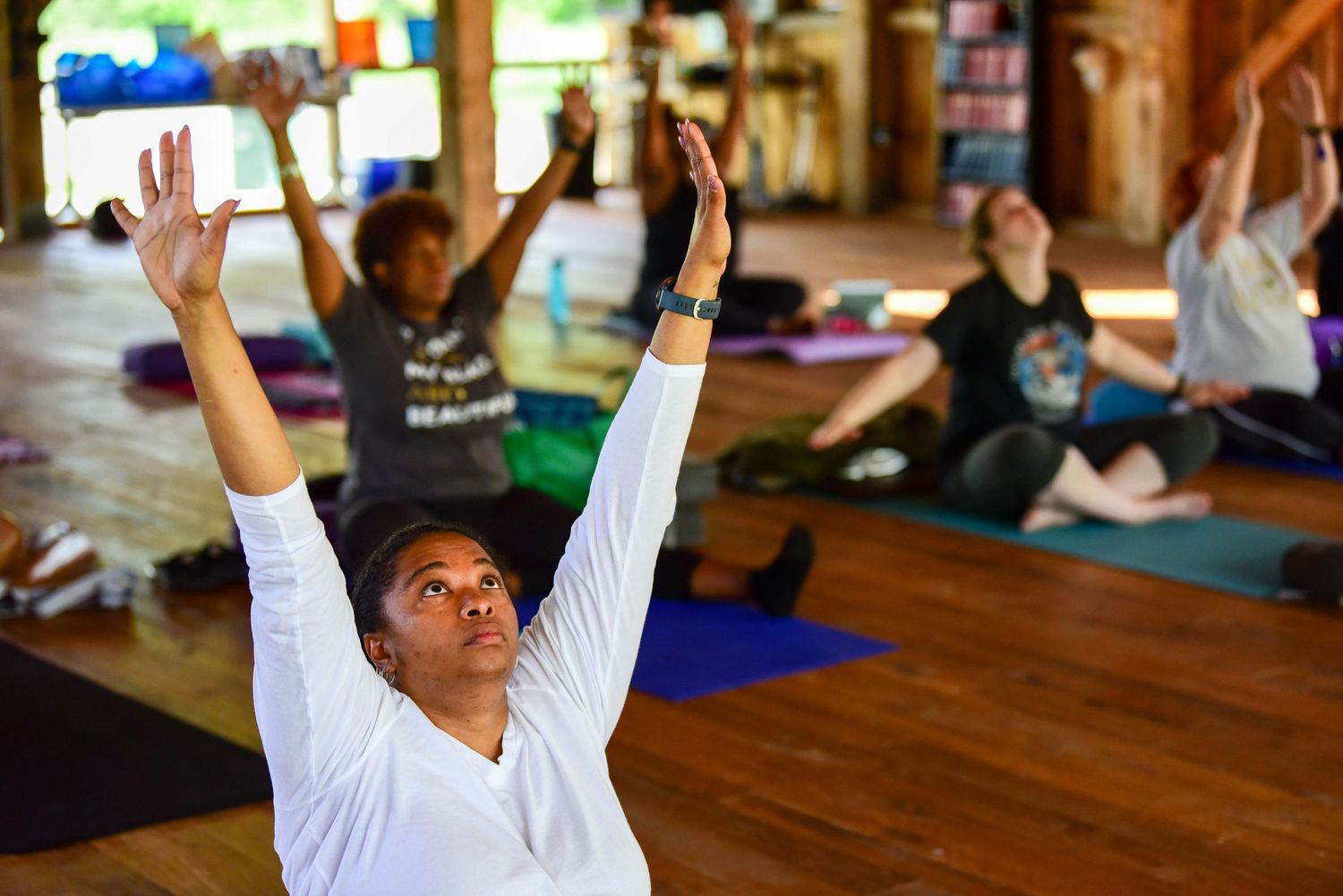 Group yoga session with participants raising arms in synchronization at a wooden studio.