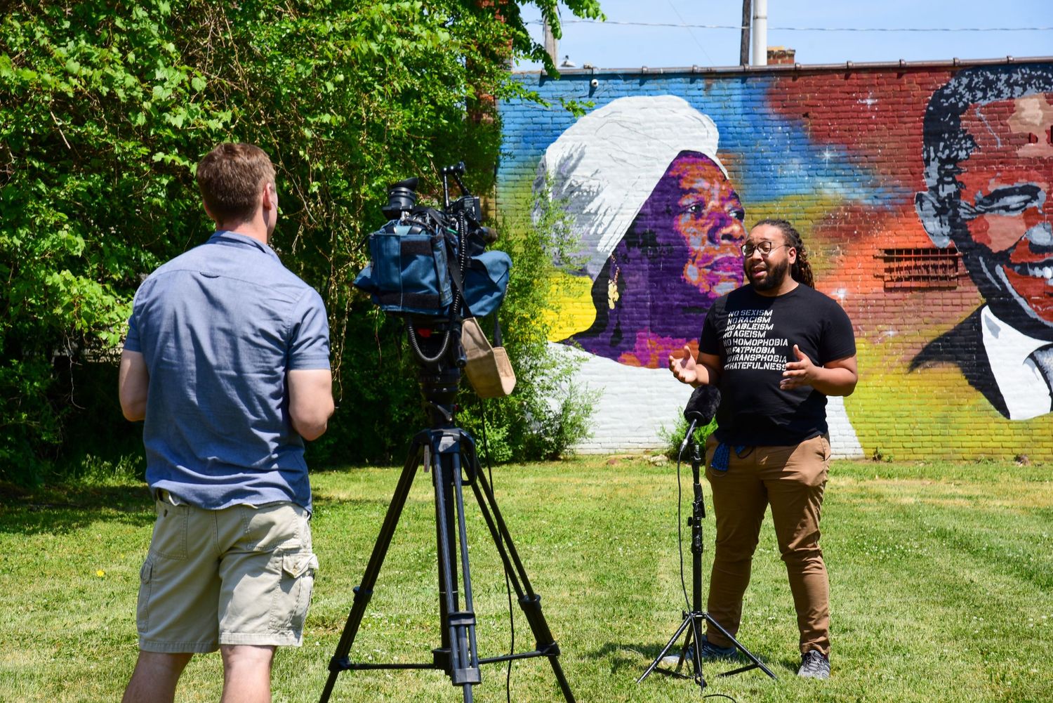 Film crew setting up equipment outdoors with colorful mural in background.