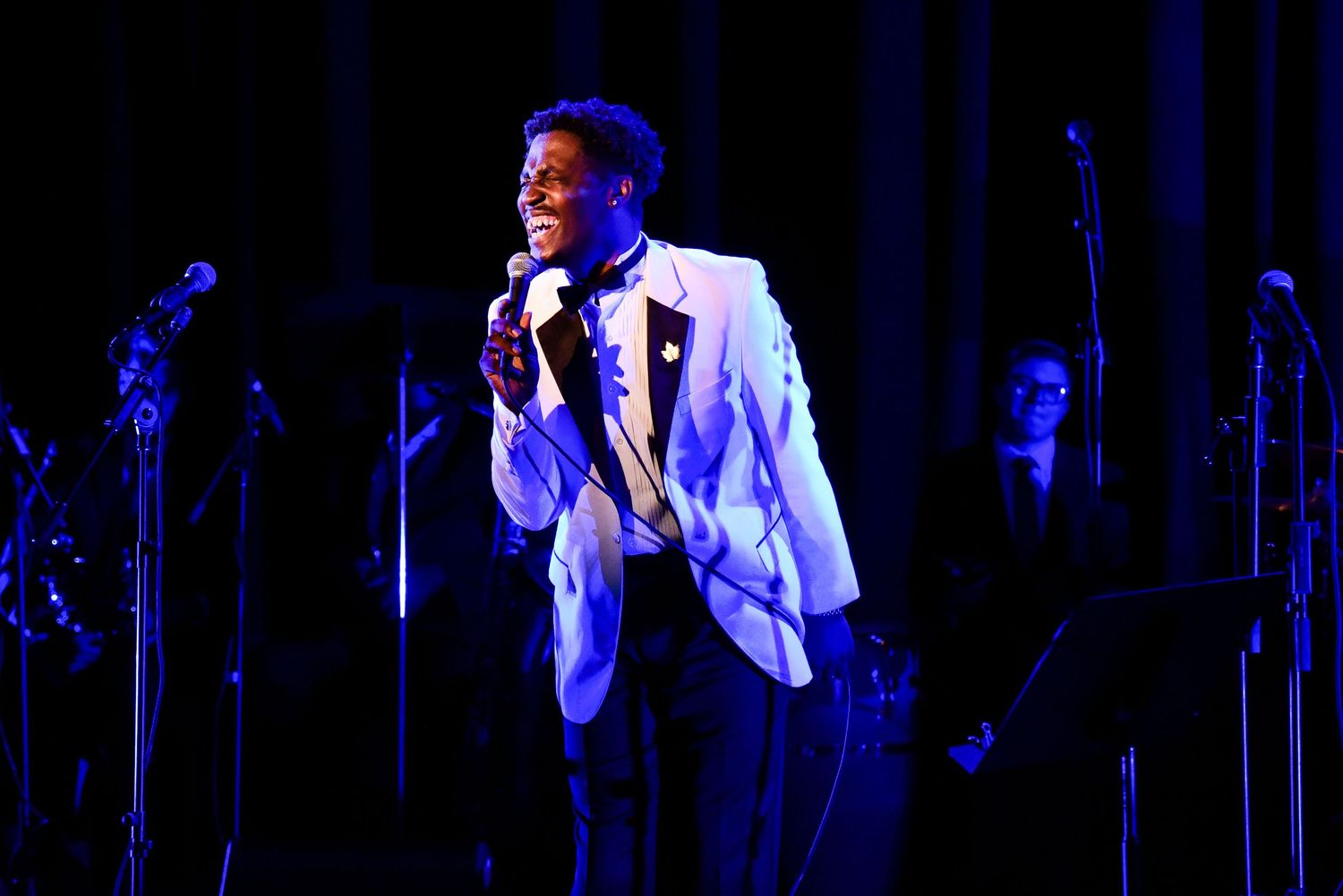 Concert performance with dramatic blue stage lighting and microphone stands.