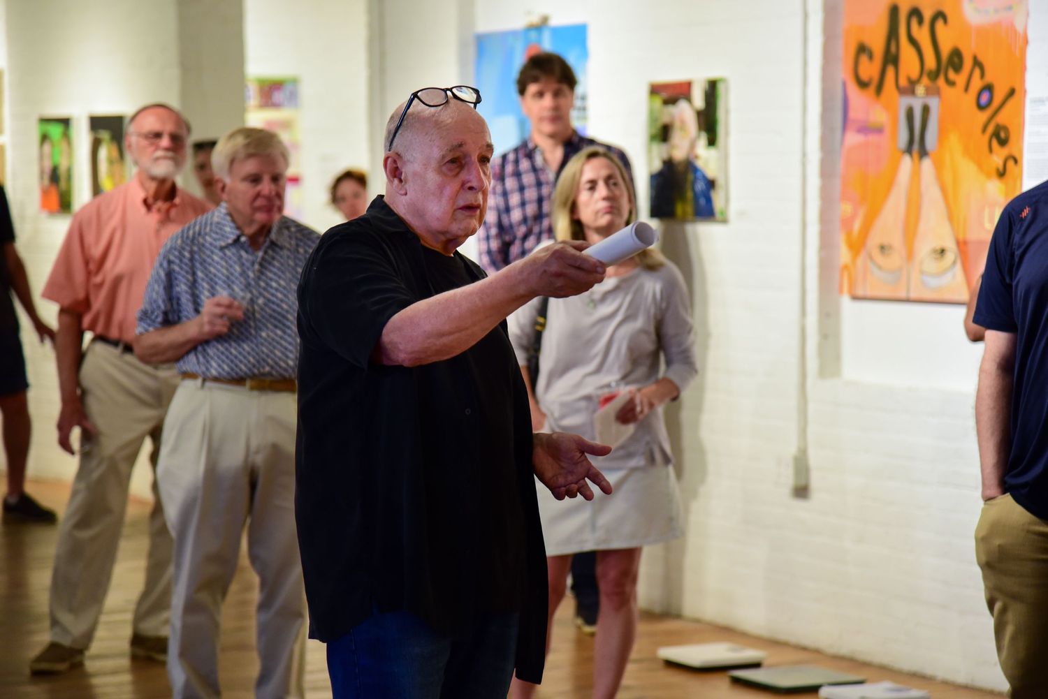 People viewing framed artwork displayed on white gallery walls.