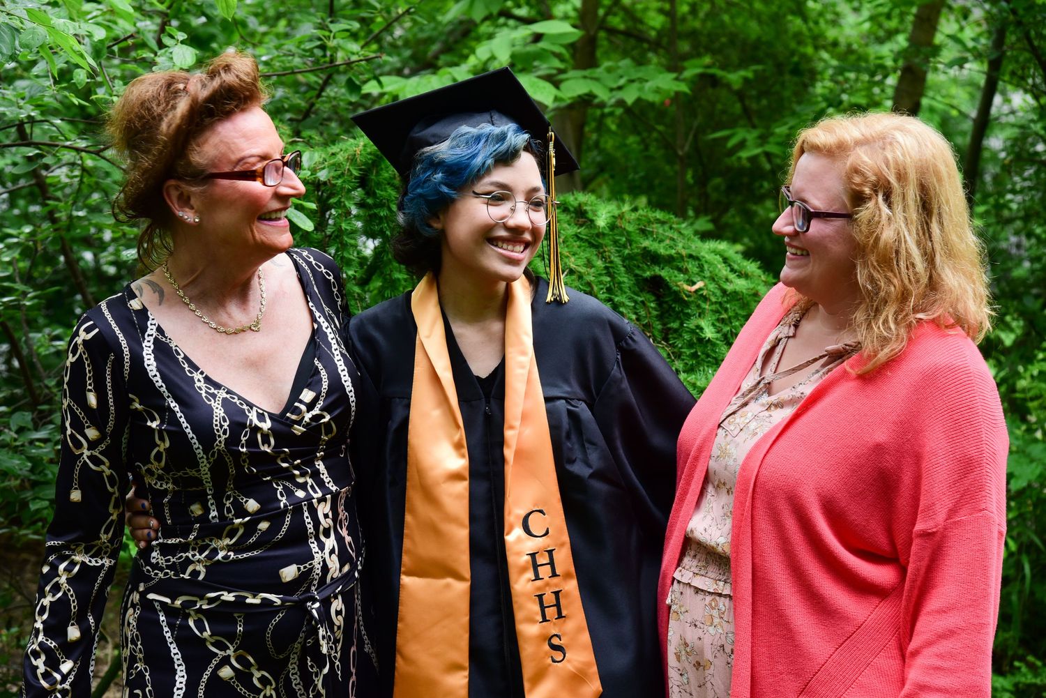 Group photo of graduates in colorful attire standing outdoors in a garden setting.