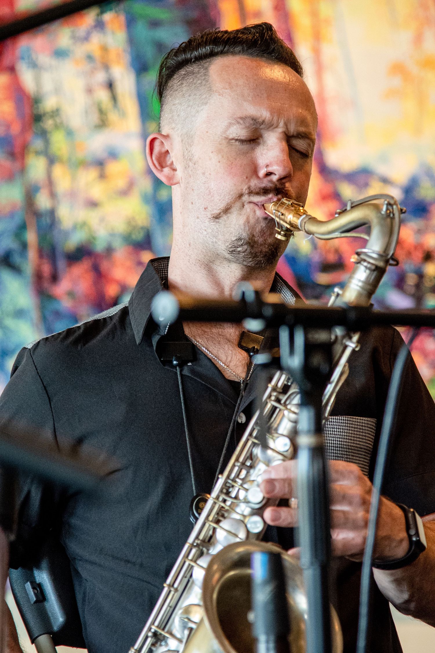 Musician playing saxophone against colorful abstract art background during performance.