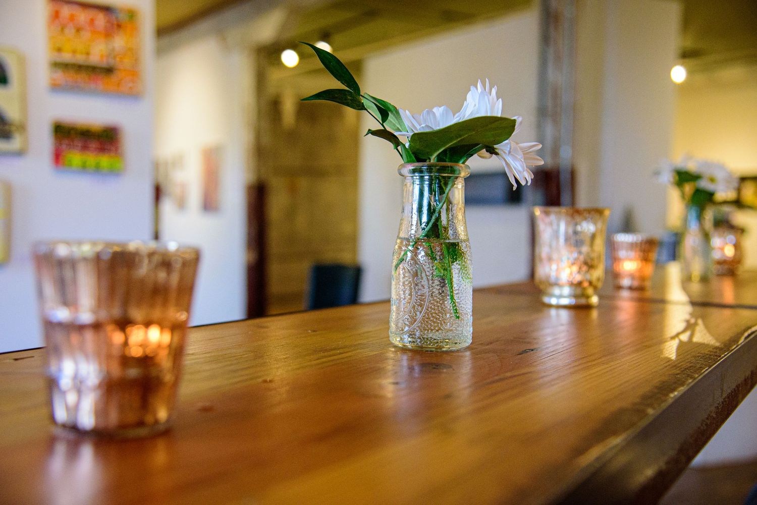 Long wooden table with glassware and small vases in a rustic indoor setting.