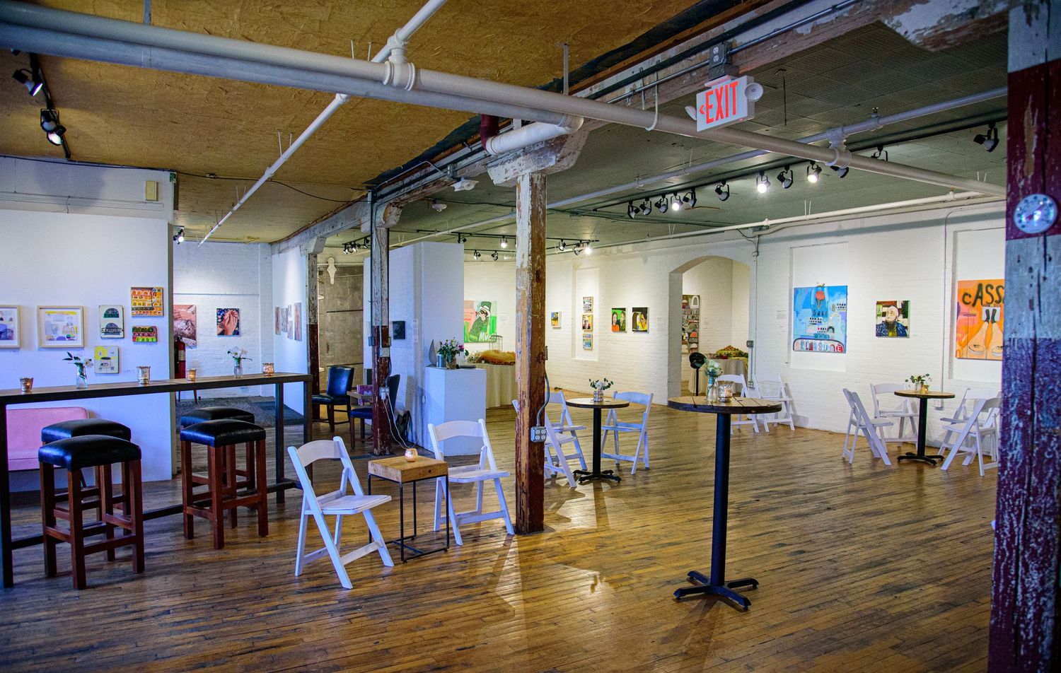 Panoramic view of an empty art gallery space with wooden floors and white walls.