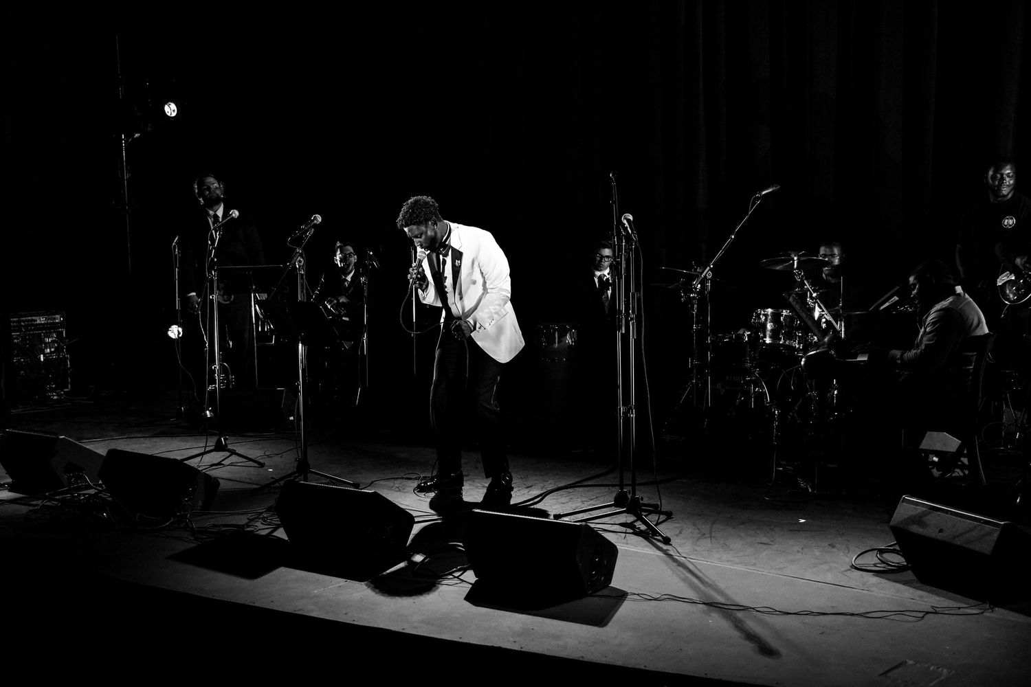 Silhouetted performer on stage with microphone stands and musical equipment in dramatic black and white lighting.