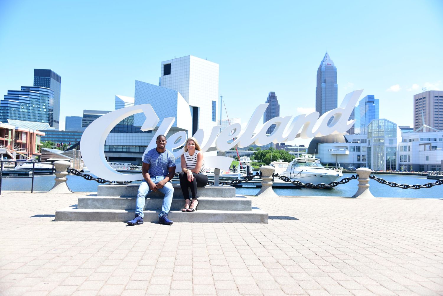 Panoramic cityscape showing modern skyscrapers against bright blue sky with pedestrians in foreground.