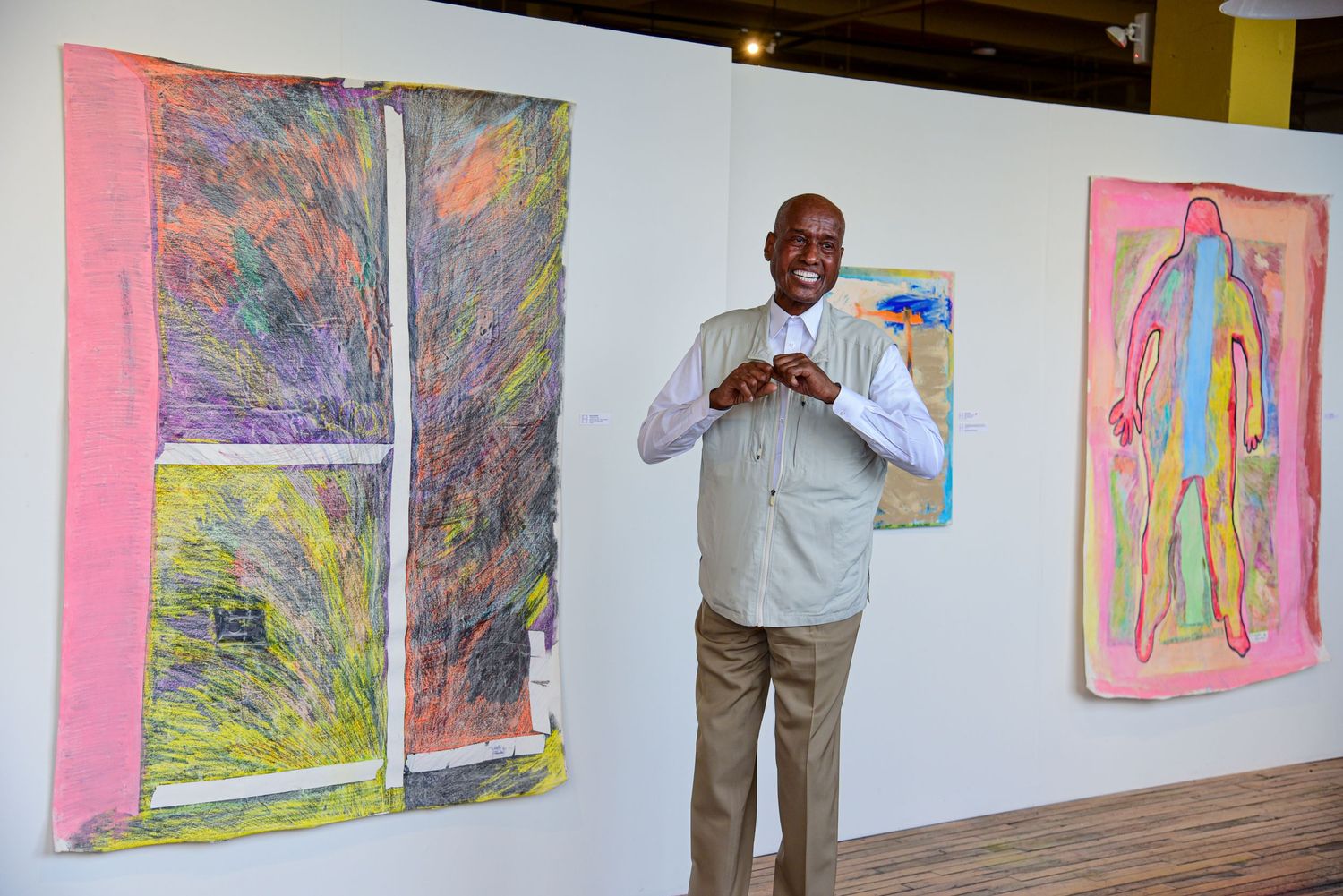 Colorful art exhibition showing abstract paintings with vibrant hues on white gallery walls.